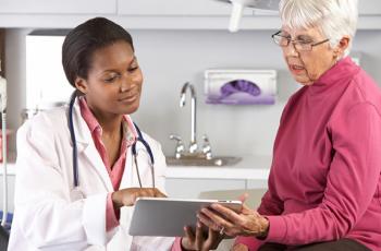 A doctor and her older patient looking at a tablet together in a doctor's office.