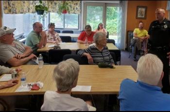 Law enforcement officer addressing room of older individuals. 