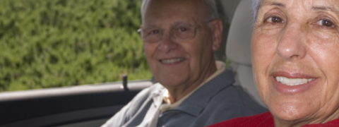 An older man and woman sitting in the car. They are smiling and the woman is sitting in the driver's seat. 