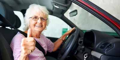 Older woman driving a car, smiling and holding her thumb up