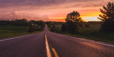 A rural road in Minnesota stretches towards the horizon and a setting sun.