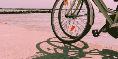 Two bicycles stand side by side on a beach casting shadows.